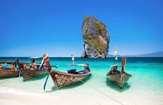 Traditional wooden boats moored on a sandy beach with a stunning rock formation in the background, inviting exploration | MSC Cruises