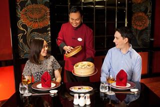 A couple enjoys dinner at the MSC Orchestra restaurant with a smiling waiter | MSC Cruises