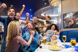 A lively group of friends enjoying a sports match together in a vibrant bar setting with drinks and laughter | MSC Cruises