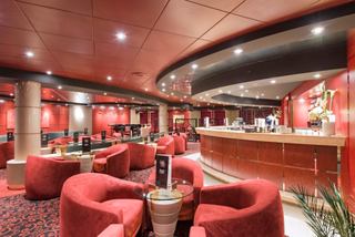 Un área de salón vibrante con cómodos asientos rojos y un acogedor mostrador de bar para relajarse y socializar | MSC Cruceros