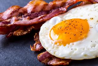 A close-up of a perfectly cooked egg with a golden yolk beside crispy bacon on a dark plate | MSC Cruises