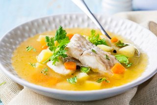 A warm bowl of fish and vegetable soup garnished with fresh herbs and served with a spoon | MSC Cruises