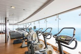 Un gimnasio luminoso lleno de equipos de fitness y grandes ventanas con vistas al mar | MSC Cruceros