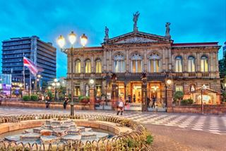 A beautiful theatre building illuminated at night, surrounded by a fountain and vibrant city life | MSC Cruises
