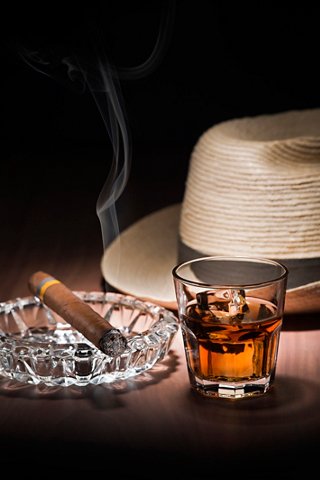 A close-up of a whiskey glass next to a cigar, ashtray, and a stylish hat, creating a sophisticated atmosphere | MSC Cruises