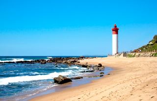 A serene beach scene featuring the Umhlanga Rocks lighthouse along a sandy coastline with gentle waves lapping the shore | MSC Cruises