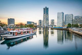 Una vista serena di una barca nell'acqua, che riflette lo skyline moderno di Yokohama, Giappone al tramonto | MSC Crociere