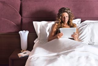 A guest enjoying leisure time in bed while using a tablet in a cabin on MSC Preziosa | MSC Cruises