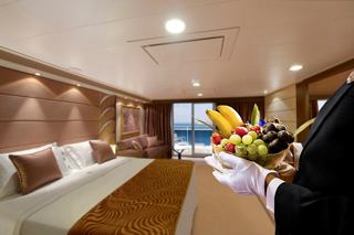 Une luxueuse suite deluxe dans le MSC Yacht Club avec un décor élégant et un majordome accueillant tenant un saladier de fruits | MSC Croisières