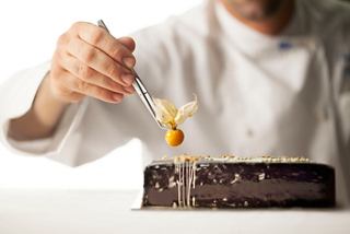 A chef delicately places a physalis fruit on a chocolate dessert, showcasing culinary artistry and precision | MSC Cruises