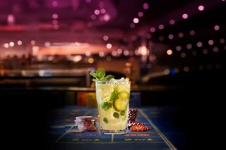 A refreshing mojito cocktail sits elegantly on a table, with a vibrant casino atmosphere in the background | MSC Cruises