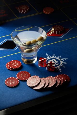 A cocktail glass with a martini and olives sits on a casino table with poker chips and dice | MSC Cruises