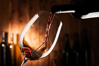 A glass being filled with red wine from a bottle against a warm background | MSC Cruises