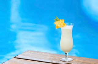 A refreshing Piña Colada garnished with pineapple sits by a shimmering pool | MSC Cruises