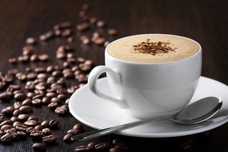 A creamy coffee served in a white cup beside scattered coffee beans and a spoon | MSC Cruises