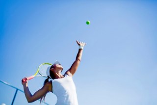 A woman serves a tennis ball against a clear blue sky while enjoying life on board | MSC Cruises