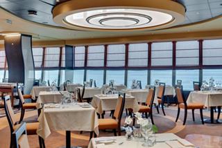 A spacious dining area with panoramic sea views, featuring elegant tables and warm decor for an inviting experience | MSC Cruises