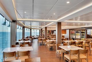 Spacious dining area with light wood furniture and large windows offering sea views | MSC Cruises