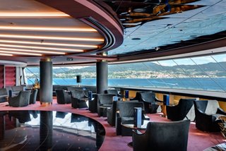 A stylish lounge area with tables and seating, offering views of the sea and coastline | MSC Cruises