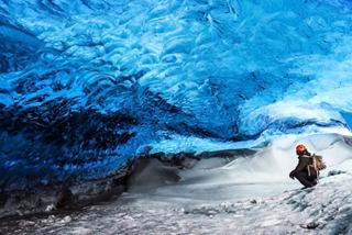 A visitor exploring the stunning ice cave in Vatnajökull National Park, surrounded by vibrant blue ice formations | MSC Cruises