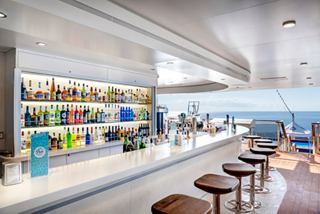 A stylish bar with colourful bottles and seating, offering stunning ocean views | MSC Cruises