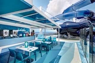 A vibrant lounge with panoramic ocean views, featuring a bar counter and seating under a bright blue canopy | MSC Cruises