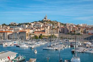 Une vue pittoresque du port de Marseille avec des bateaux, surplombant la ville et son église historique au sommet de la colline | MSC Croisières