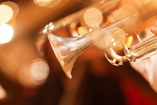 A close-up of a hand holding a trumpet against a blurred, warm background, celebrating music and entertainment | MSC Cruises