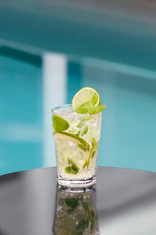A refreshing mojito cocktail served in a glass, garnished with mint and lime, set against a vibrant blue background | MSC Cruises