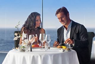 A couple enjoying a meal at a table by the sea, with a beautiful view from the MSC Preziosa | MSC Cruises
