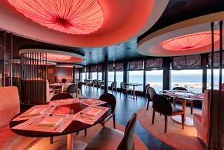 Un restaurante bellamente diseñado con ventanas panorámicas y una cálida iluminación crea un ambiente acogedor | MSC Cruceros