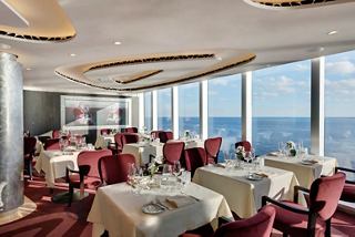 Elegant dining area in the MSC Yacht Club with sea views, featuring tables and warm décor | MSC Cruises