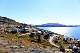 A scenic view of Qaqortoq's coastline, featuring houses along the sea under a clear blue sky | MSC Cruises