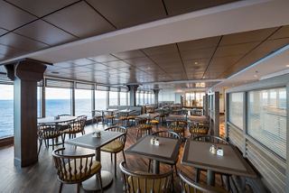 A bright dining area with tables and chairs, offering stunning views of the sea through large windows | MSC Cruises