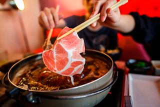 Una persona sostiene palillos con carne finamente cortada sobre una olla humeante llena de sopa | MSC Cruceros