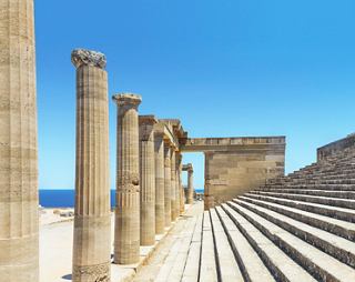 Ancient ruins with columns at an archaeological site in Lindos, Rhodes, set against a bright blue sky and sea | MSC Cruises