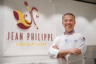 El renombrado chef pastelero Jean-Philippe Maury se encuentra orgulloso frente al cartel de su café en MSC Meraviglia | MSC Cruceros