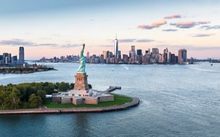 The Statue of Liberty stands tall in the foreground with the New York City skyline at dusk in the background | MSC Cruises