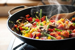 A vibrant wok filled with colourful vegetables, mushrooms and tomatoes, steaming and ready to be served | MSC Cruises