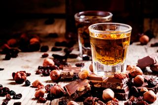 A close-up of a glass of liquor surrounded by chocolate, nuts, and dried fruits on a table | MSC Cruises