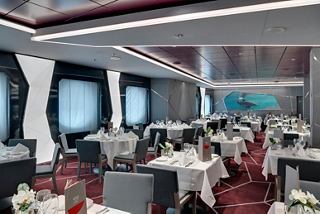 A spacious restaurant on MSC Seaview featuring elegant tables and chairs with large porthole windows | MSC Cruises