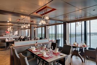 A beautifully arranged restaurant with large windows offering a scenic view and inviting ambiance for diners | MSC Cruises
