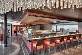 A vibrant dining area featuring the Asian Market Kitchen by Roy Yamaguchi, showcasing a sushi bar and warm seating | MSC Cruises