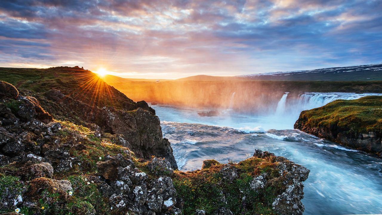 A breathtaking view of a river cascading through lush green hills under a vibrant sunrise in Iceland | MSC Cruises