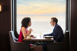 Un couple apprécie un repas ensemble avec une vue mer à couper le souffle à travers un hublot sur MSC Meraviglia | MSC Croisières