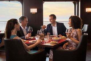 Un grupo de amigos disfruta de una comida juntos en un elegante restaurante con vista al mar en el MSC Meraviglia | MSC Cruceros