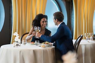 Una pareja brinda con vino en un restaurante a bordo del MSC Meraviglia, con una vista impresionante al mar a través del porthole | MSC Cruceros
