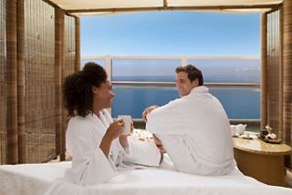 Ein Paar genießt einen entspannenden Moment in einer Spa-Cabana mit Blick auf das Meer, eingehüllt in Bademäntel und einen Drink teilend | MSC Cruises