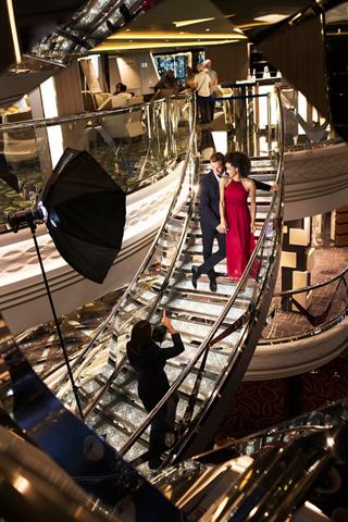 Una pareja navega por la elegante escalera del MSC Meraviglia, rodeada de cálida iluminación y atentos miembros de la tripulación | MSC Cruceros