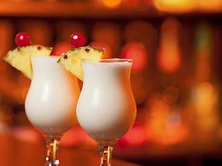 Two refreshing Piña Colada cocktails garnished with pineapple and cherries, set against a warm bar backdrop | MSC Cruises